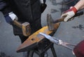 Blacksmith hands holding forceps and a hammer forging a metal billet, blade of a knife, on an anvil