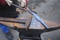 Blacksmith hands holding forceps and a hammer forging a metal billet blade of a knife on an anvil