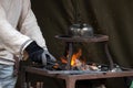 Blacksmith heating up metal in red hot coals while tea pot boiling water on top. Craftsman hand forging metal, red sparks are