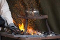 Blacksmith heating up metal in red hot coals while tea pot boiling water on top. Craftsman hand forging metal, red sparks are