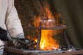 Blacksmith heating up metal in red hot coals while tea pot boiling water on top. Craftsman hand forging metal, red sparks are