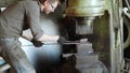 Blacksmith holding candent iron ingot and forging it using pneumatic hammer.