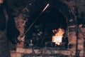 Blacksmith holding glowing molten sword near brick furnace in forge. Farrier in dirty working clothes crafting iron.