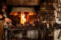 blacksmith holds billet over hot coals in clay oven. blacksmith heating iron metal sword manufacturing marching forge,