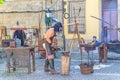Blacksmith man forging iron metal in cobblestone square with medieval houses and buildings