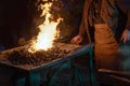 Blacksmith at work at the forge fire, working hands, some iron bars and the burning coal against a dark background