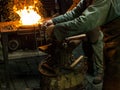 A blacksmith works with metal close to open fire
