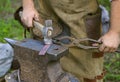 Blacksmiths hands holding forceps and hammer forging a metal billet, blade of a knife, on an anvil Royalty Free Stock Photo