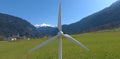 The blades of an industrial wind turbine against the backdrop of a mountain village. Renewable energy plus self-contained power