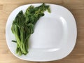 Blanched vegetable are placed on the left side of board on a white plate on a brown wooden. Royalty Free Stock Photo