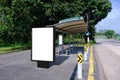 Blank advertising poster banner mockup at empty bus stop shelter by main road, greenery behind; out-of-home OOH vertical billboard Royalty Free Stock Photo