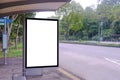 _Blank advertising poster banner mockup template at empty bus stop shelter by main road. Greenery around vertical out-of-home OOH Royalty Free Stock Photo