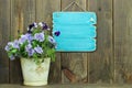 Blank antique blue sign by pot of purple flowers (pansies)