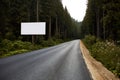 Blank billboard sign by empty highway through forest mountains landscape. Ad panel on road. Royalty Free Stock Photo