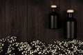 Blank black cosmetics bottles with white small flowers on dark wood board, mock up, top view.