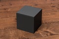 Blank black cube gift box with closed hinged flap lid on dark wooden background. Clipping path around box mock up.