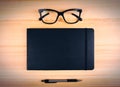 Blank black diary with eyeglasses and pen on wooden table, mock