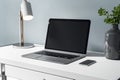 Blank black laptop display with modern lamp and and smartphone on white table for remote work. Mockup