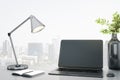 Blank black laptop monitor on office table with stylish lamp, notebook and black glass vase on city view background. Mockup