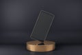 Blank black smartphone display standing on one corner on golden cylinder at abstract dark background. Realistic cell phone mockup Royalty Free Stock Photo