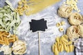 Blank blackboard label among mixed types and shapes of italian pasta on grey stone, background