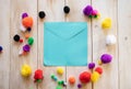 Blank blue envelope surrounded by multi-coloured pom poms