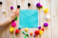 Blank blue envelope surrounded by multi-coloured pom poms