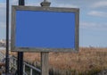 Blank blue faced sign with a wooden frame on a post on a boardwalk by brown tall grass covering a sand dune on a beach Royalty Free Stock Photo