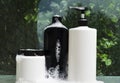 Blank bottles of beauty products, foam on it standing on the wet glass shelf against green plants