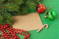 Blank brown greeting card, two christmas balls, red bead garland and spruce branch on a textured green background. Winter season Royalty Free Stock Photo