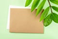 Blank brown paper card and fresh green leaves of eternity Zuzu plant or Zamioculcas zamiifolia on a pastel green background.