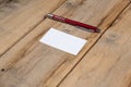 A blank business card and a red pen against a wooden background. A white paper rectangle and a ballpoint pen lie on top of old Royalty Free Stock Photo