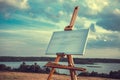 Blank canvas rests on a easel on lake landscape.