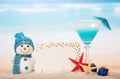 Blank card, cocktail, snowman and gifts in sand against sea.