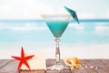 Blank card, cocktail, starfish and shell in sand against sea. Royalty Free Stock Photo