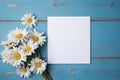 blank card mockup on blue wooden background surrounded by bouquet daisies flowers, template white sheet of paper for design Royalty Free Stock Photo