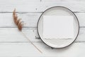 Blank card mockup on a plate and beige reed on a white wooden table. Stylish scene for a blogger. Top view, flat lay