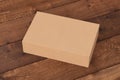 Blank cardboard wide flat box with closed hinged flap lid on dark wooden background.