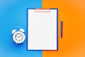 Blank clipboard mock-up, a blue pen and white alarm clock on the blue-orange color background. Top view, copy space. Back to Royalty Free Stock Photo