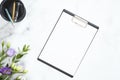 Blank clipboard mockup, stationery, flowers bouquet on marble background. Flat lay, top view minimalistic home office desk. Royalty Free Stock Photo