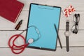 blank clipboard, pills, book, stethoscope, eyeglasses and watch on wooden background