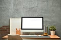 Blank computer monitor, picture frame, books, pencil holder and houseplant on wooden table against concrete wall Royalty Free Stock Photo