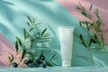 A blank cosmetic tube mockup stands among olive branches with a serene pastel backdrop.