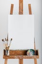 Blank white art canvas sitting on wooden artist easel with paintbrushes in a jar Royalty Free Stock Photo