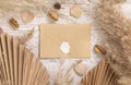 Blank envelope on white wooden table near dried plants, palm leaves, pampas grass and hearts