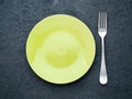 Blank flat yellow plate, fork on dark gray stone concrete table, top view. Mock up, copy space