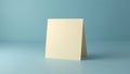 Blank folded card stands upright on light blue surface. Clean minimal studio backdrop for your message. Beige card offers ample Royalty Free Stock Photo