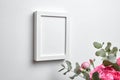 Blank frame mockup hanging on white wall and pink flowers in interior. White frame and floral decor Royalty Free Stock Photo