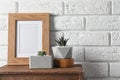 Blank frame and succulent plants on wooden  near white brick wall, space for design. Home decor Royalty Free Stock Photo