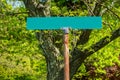 Blank green street sign on a rusty metal pole with green leaves and a tree in the background Royalty Free Stock Photo